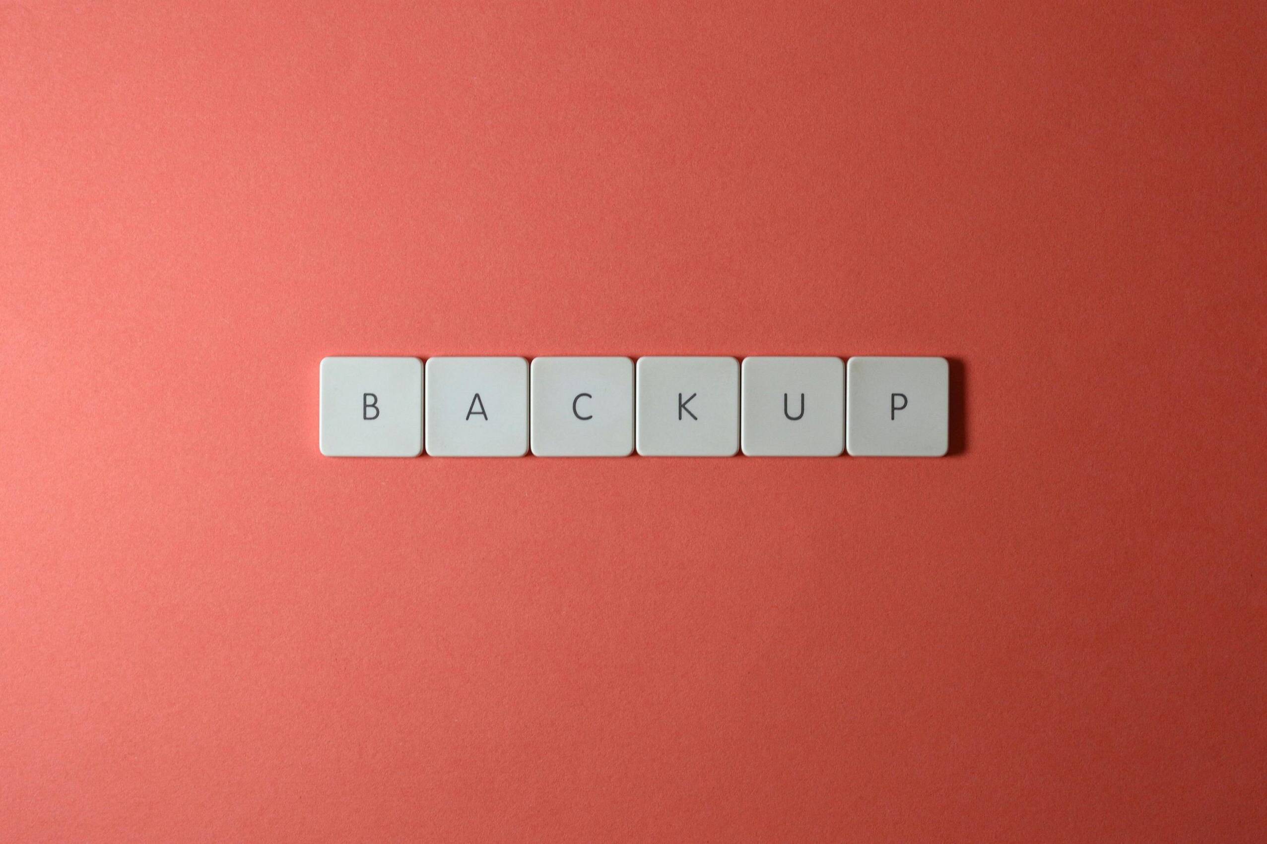 Free Close-up of keyboard keys spelling 'BACKUP' placed on a coral-colored surface. Stock Photo